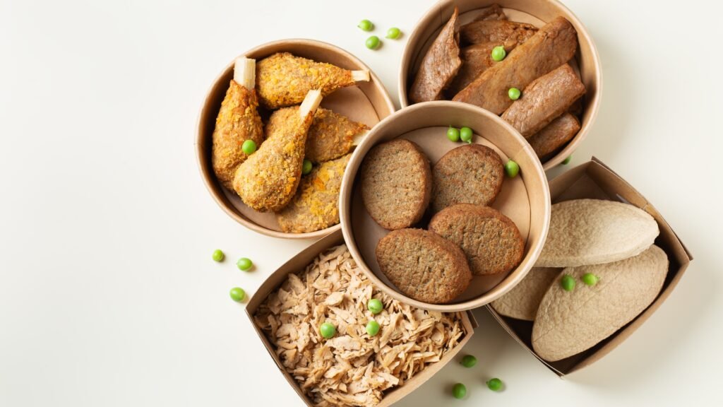 Une sélection d'alternatives protéines végétales à la viande dans des bols en carton, comprenant des nuggets, des galettes, des tranches de seitan et des miettes de viande végétale.